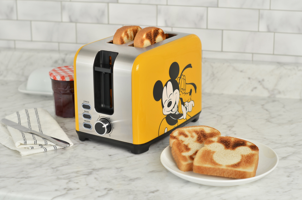 Mickey and Pluto 2-slice toaster in yellow color with stainless steel accents shown with golden brown toast on a plate