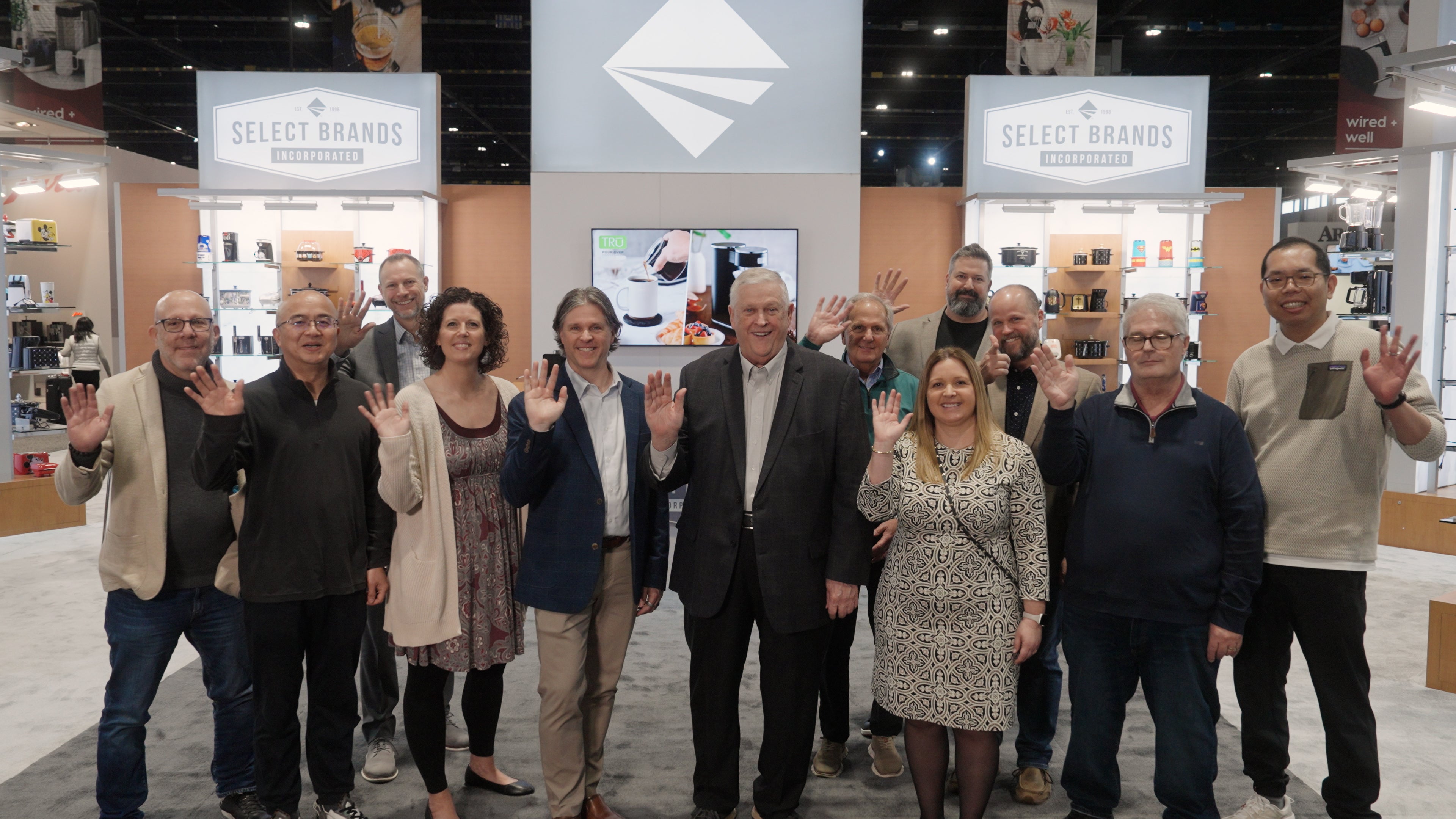 The Select Brands team at a trade show, waving and smiling